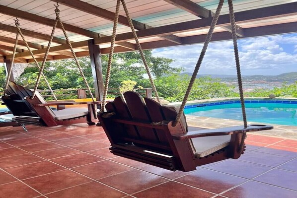 Un espacio al aire libre techado con dos sillones de madera y una piscina.