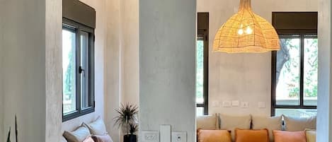 A modern interior with arched windows, a hanging light fixture, a seating area with cushions, and potted plants.