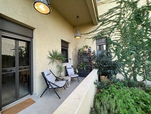 An outdoor seating area with chairs and a table, a hanging light fixture, and a wall with climbing plants. - Artisan Duplex • Talpiot Market by SeaNRent (Tiberias)