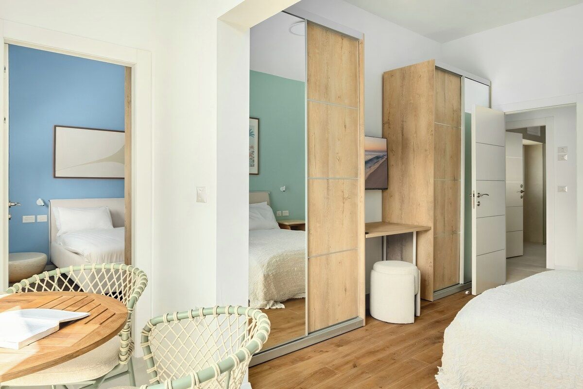 A modern bedroom with a bed, a wooden wardrobe, a mirror, and a seating area with a table and chairs.