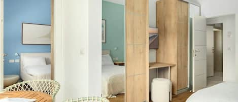 Un dormitorio moderno con cama, armario de madera, espejo y zona de estar con mesa y sillas.