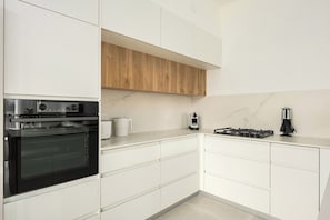 A modern kitchen with white cabinetry, a built-in oven, a coffee maker, and a gas stove.