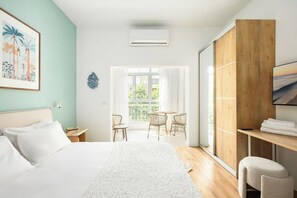 A hotel room with a bed, a desk, a chair, a balcony with a view, and an air conditioning unit.