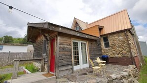 A rustic cabin with a wooden exterior, a red door, and a stone wall. - CC62-Davis Cottage, Walk to shops! Firepit! Pets Ok! A/C (Davis)