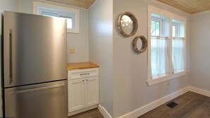 A kitchen with a stainless steel refrigerator, white cabinets, and a wooden countertop. There are two windows with white curtains and a mirror on the wall. - CC62-Davis Cottage, Walk to shops! Firepit! Pets Ok! A/C (Davis)