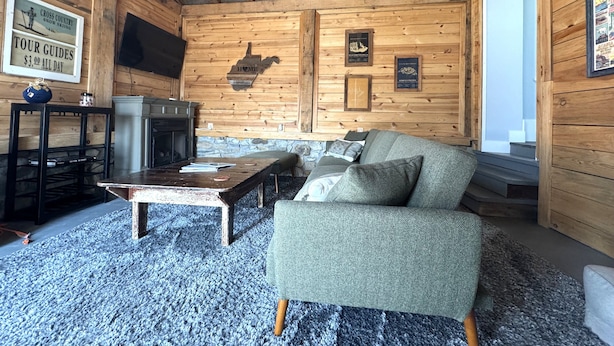 A cozy cabin interior with a wooden ceiling, a stone fireplace, a sofa, and a television mounted on the wall. - CC62-Davis Cottage, Walk to shops! Firepit! Pets Ok! A/C (Davis)