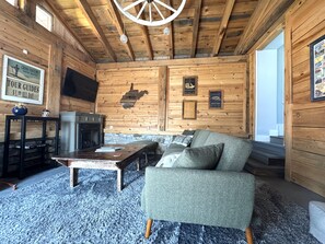A cozy cabin interior with a wooden ceiling, a stone fireplace, a sofa, and a television mounted on the wall. - CC62-Davis Cottage, Walk to shops! Firepit! Pets Ok! A/C (Davis)