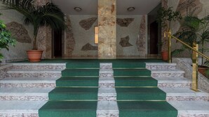 Un magnifique escalier, avec des marches recouvertes d’une moquette verte, menant à un plafond très haut.