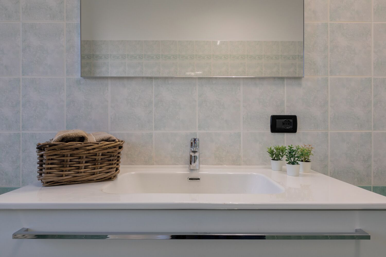 A bathroom with a white sink, a mirror above it, and a small potted plant on the counter.
