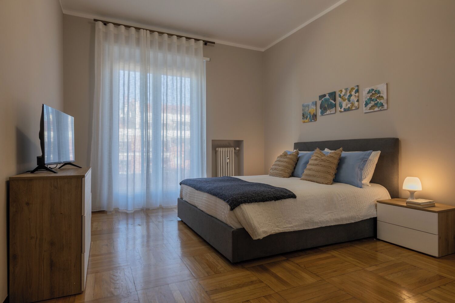 A bedroom with a bed, bedside table, lamp, and a TV on a wooden stand.