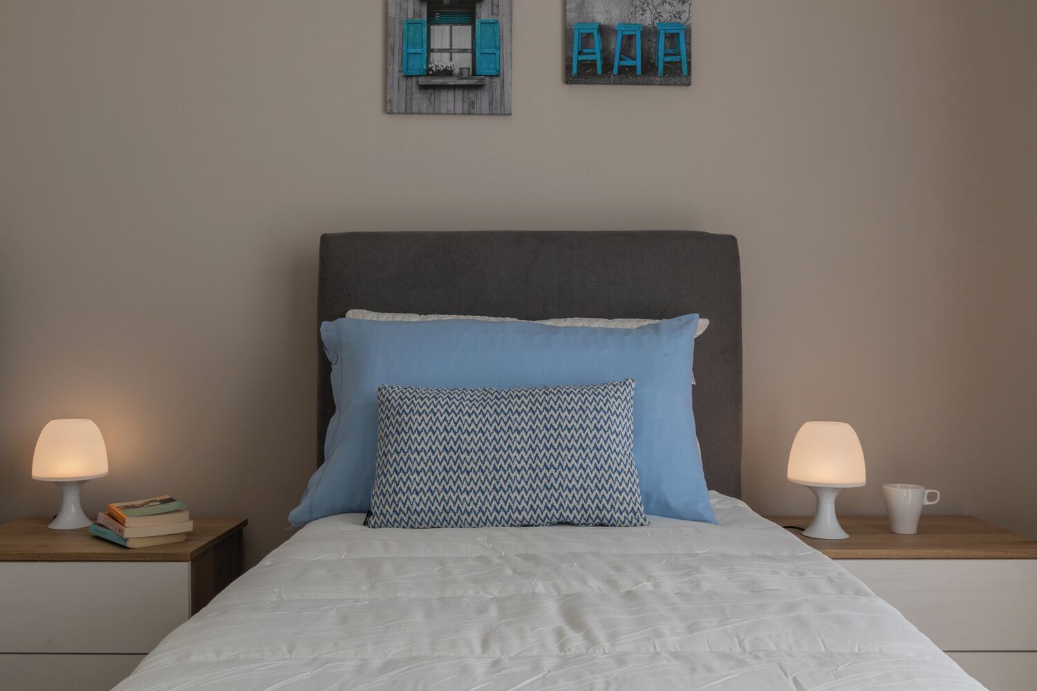 A bedroom with a bed, two bedside tables, two lamps, and a wall decoration.