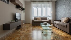 Un salon moderne doté d’un téléviseur à écran plat, de deux canapés, d’une table basse en verre et d’un mur orné d’un motif décoratif.