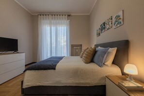 Une chambre à coucher moderne avec un lit, une télévision, une table de chevet et des œuvres d’art accrochées au mur.