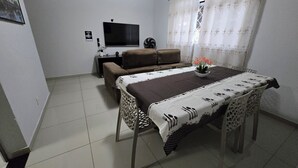 A living room with a sofa, a TV, a dining table with a patterned tablecloth, and a potted plant. - Beautiful Apartment Near VG Shopping Mall (Várzea Grande)