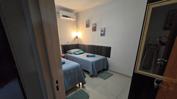 A room with two beds, a wall-mounted air conditioner, a nightstand, and a wall-mounted lamp. - Beautiful Apartment Near VG Shopping Mall (Várzea Grande)