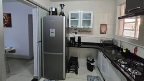 A compact kitchen with a refrigerator, a coffee maker, and a gas stove. - Beautiful Apartment Near VG Shopping Mall (Várzea Grande)