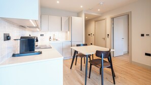 A modern kitchen with a coffee machine, a dining table with chairs, and a hallway leading to a door. - Stylish One-Bed Retreat (London)