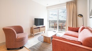 A modern living room with a sofa, armchair, TV, and a wooden cabinet. - Stylish One-Bed Retreat (London)
