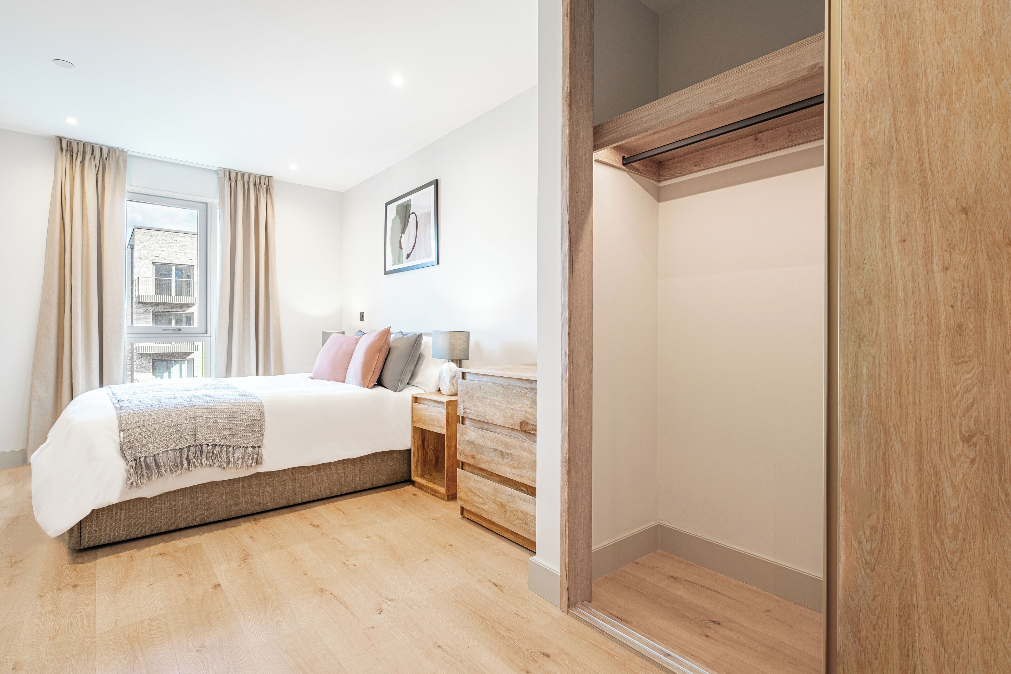 A modern bedroom with a large bed, wooden headboard, and a nightstand with a lamp.