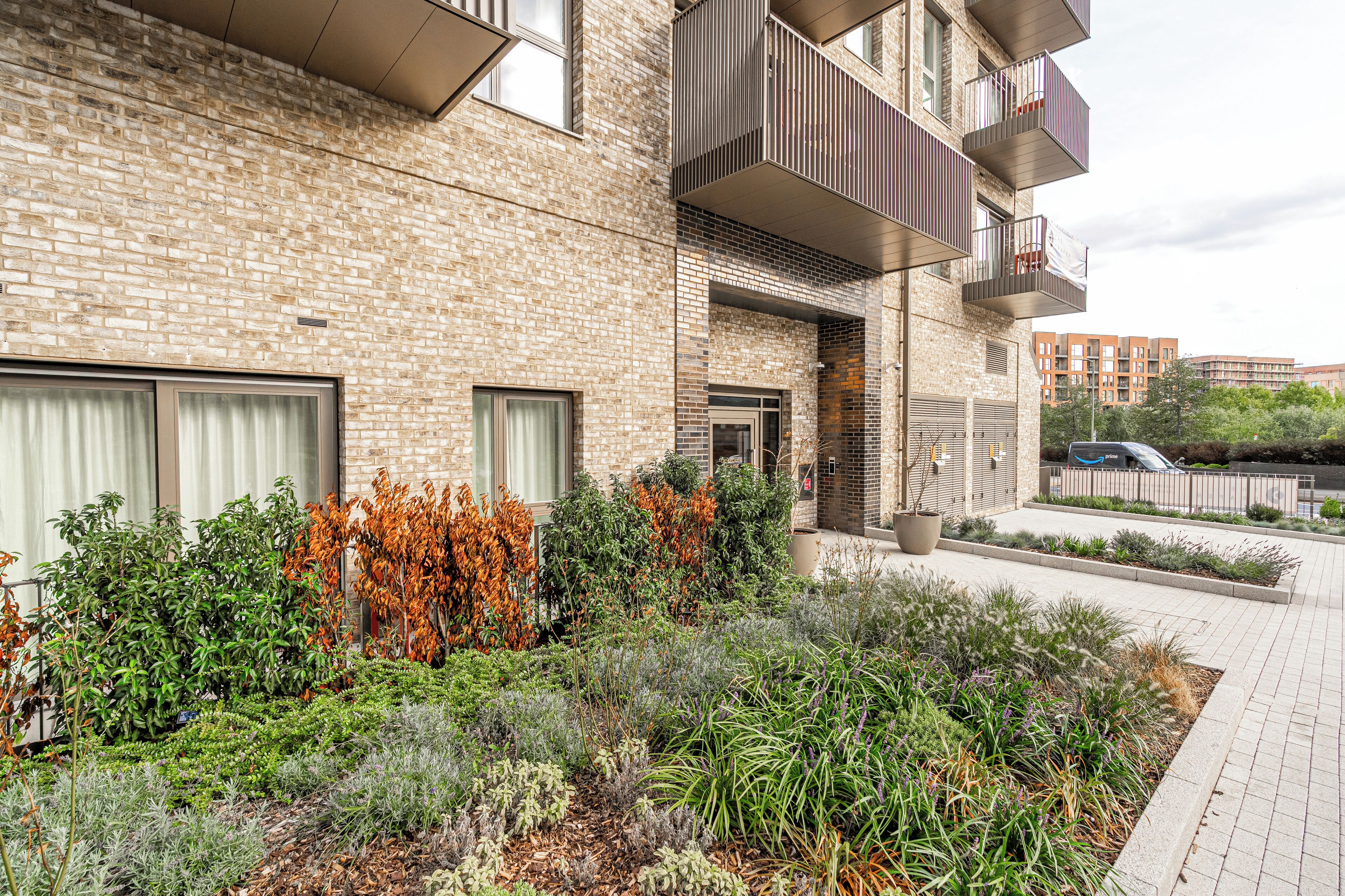 A modern building with a brick facade, balconies, and a landscaped garden area.
