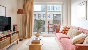 A modern living room with a sofa, a coffee table, a TV, and a balcony with a view of buildings. - Light and Space Retreat (London)