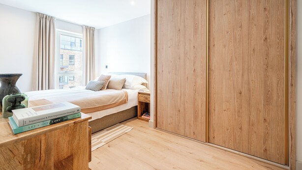 A modern bedroom with a large bed, wooden wardrobe, and a bedside table with books. - Light and Space Retreat (London)