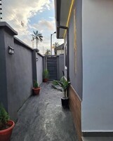 Um beco estreito e pavimentado com plantas em vasos, portão e um edifício com fachada cinzenta e detalhes em madeira.