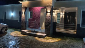 A modern house with a paved entrance, a red brick wall, and a car parked outside. - The Olive Place (Jos)