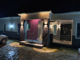 Uma casa moderna com entrada pavimentada, um muro de tijolos vermelhos e um carro estacionado na frente.
