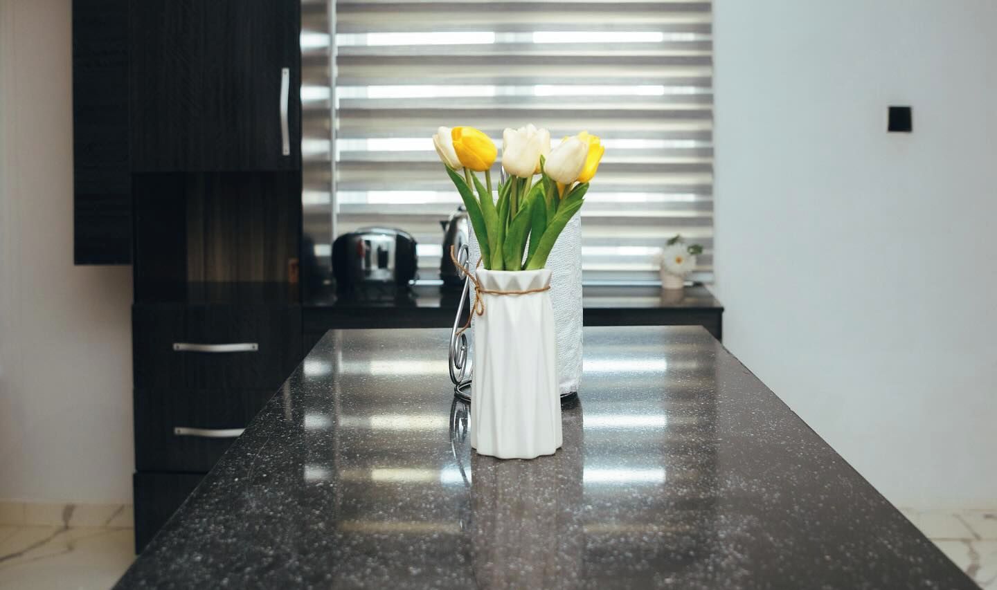En køkkenbordplade med en hvid vase med gule og hvide tulipaner.