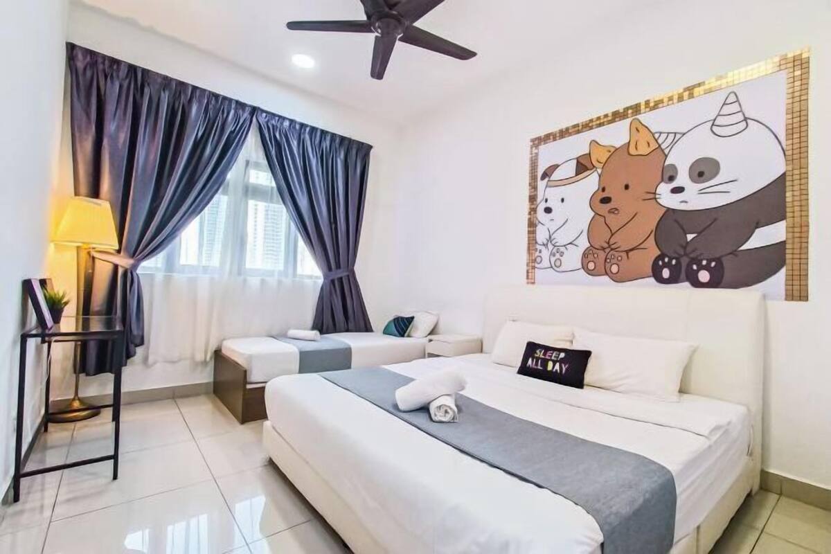 Habitación de hotel con dos camas, ventilador de techo, un cuadro con dibujos animados de animales, una lámpara y un cartel que dice 'SLEEP ALL DAY'.