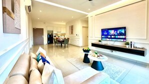 Una sala de estar moderna con sofá, mesa de centro y televisor. Se observa una cocina al fondo.