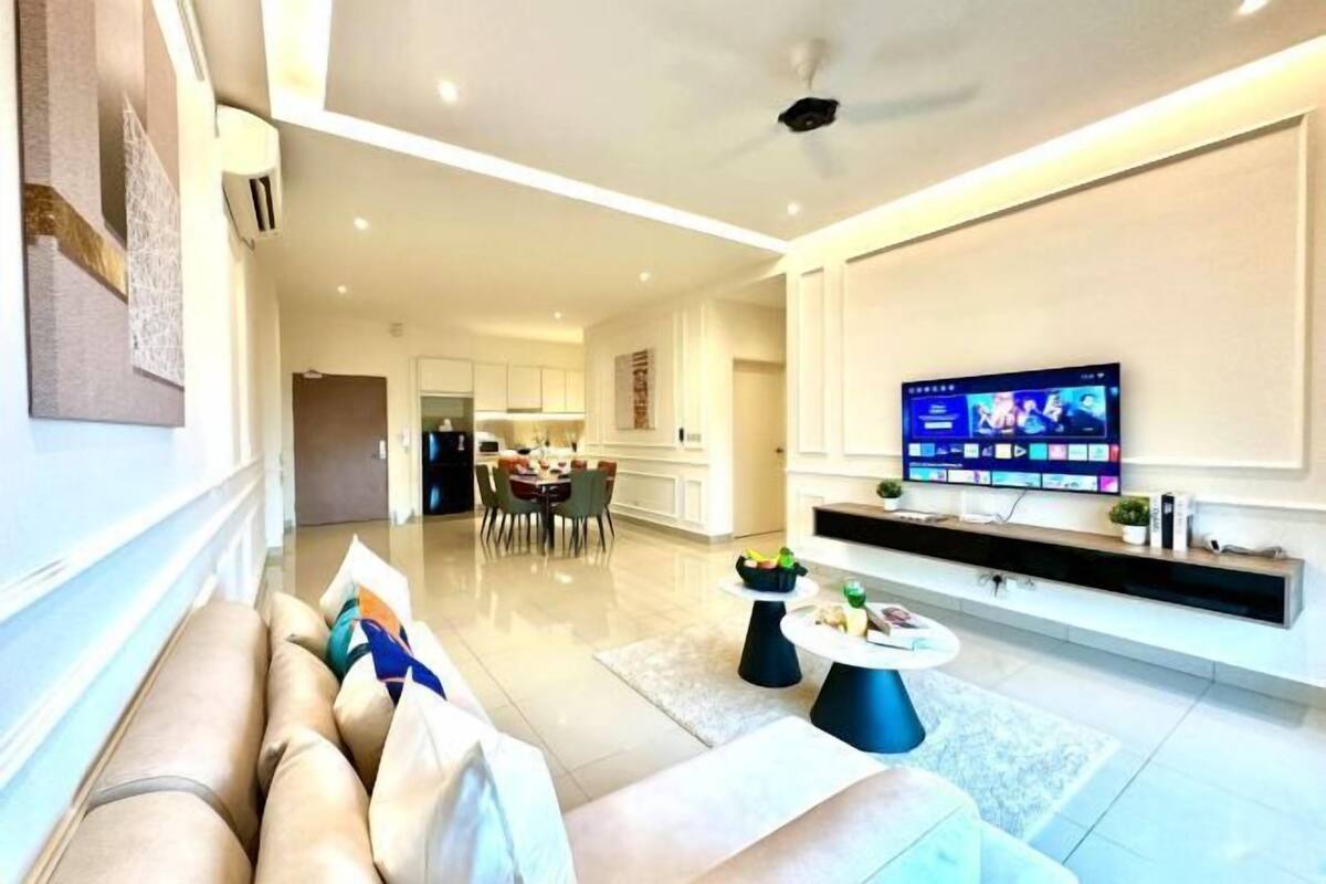 Una sala de estar moderna con sofá, mesa de centro y televisor. Se observa una cocina al fondo.