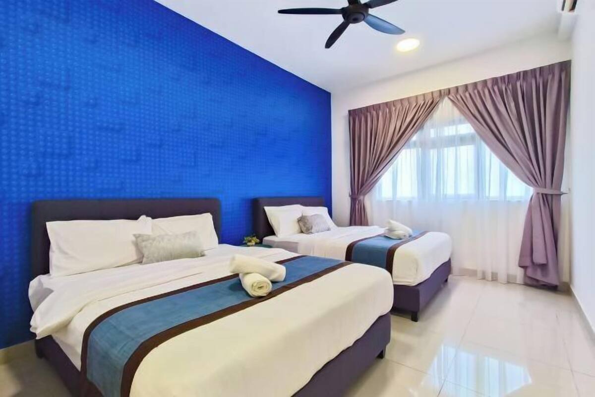 Habitación de hotel con dos camas, ventilador de techo y un amplio ventanal con cortinas.