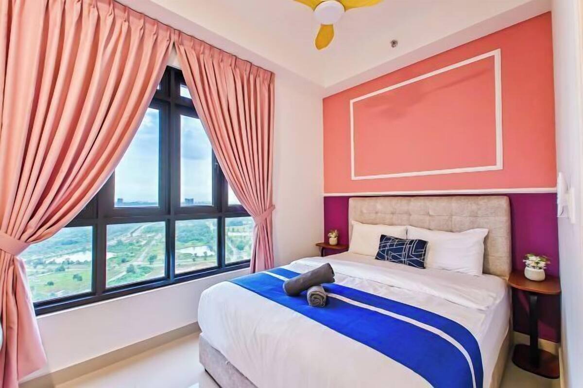 Un dormitorio con una cama, una ventana con cortinas, un ventilador de techo y una mesita de noche con lámpara.