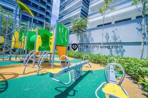 Un'area giochi all'aperto con diverse strutture ricreative, tra cui scivoli e strutture per arrampicata, adiacente a un edificio con un cartello che riporta 'JB City Homestay'.