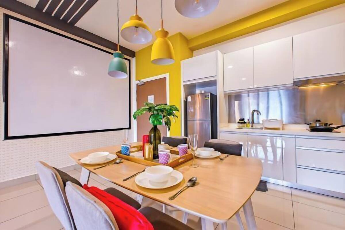 Una cocina moderna con armarios blancos, un refrigerador de acero inoxidable y un comedor con mesa dispuesta para dos.