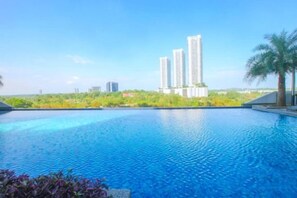 A swimming pool with a cityscape view, surrounded by greenery and palm trees. - Pangsapuri Meridian by RR JBcity (Iskandar Puteri)