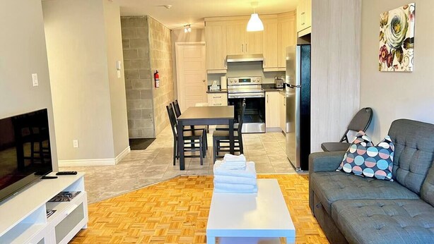 A modern living room with a flat-screen TV, a sofa, and a dining area with chairs and a table. - Central 2BR | Near Metro & Parks (Montréal)