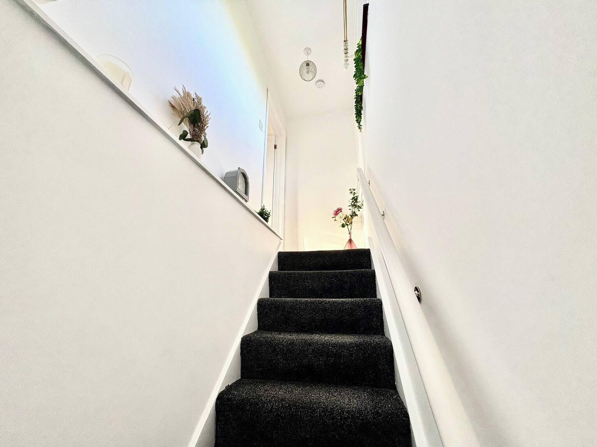 Un estrecho pasillo con paredes blancas y una escalera que sube.