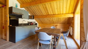 Un intérieur en bois comprenant une table et des chaises, un coin cuisine avec des placards et des appareils électroménagers, et une fenêtre laissant entrer la lumière naturelle.