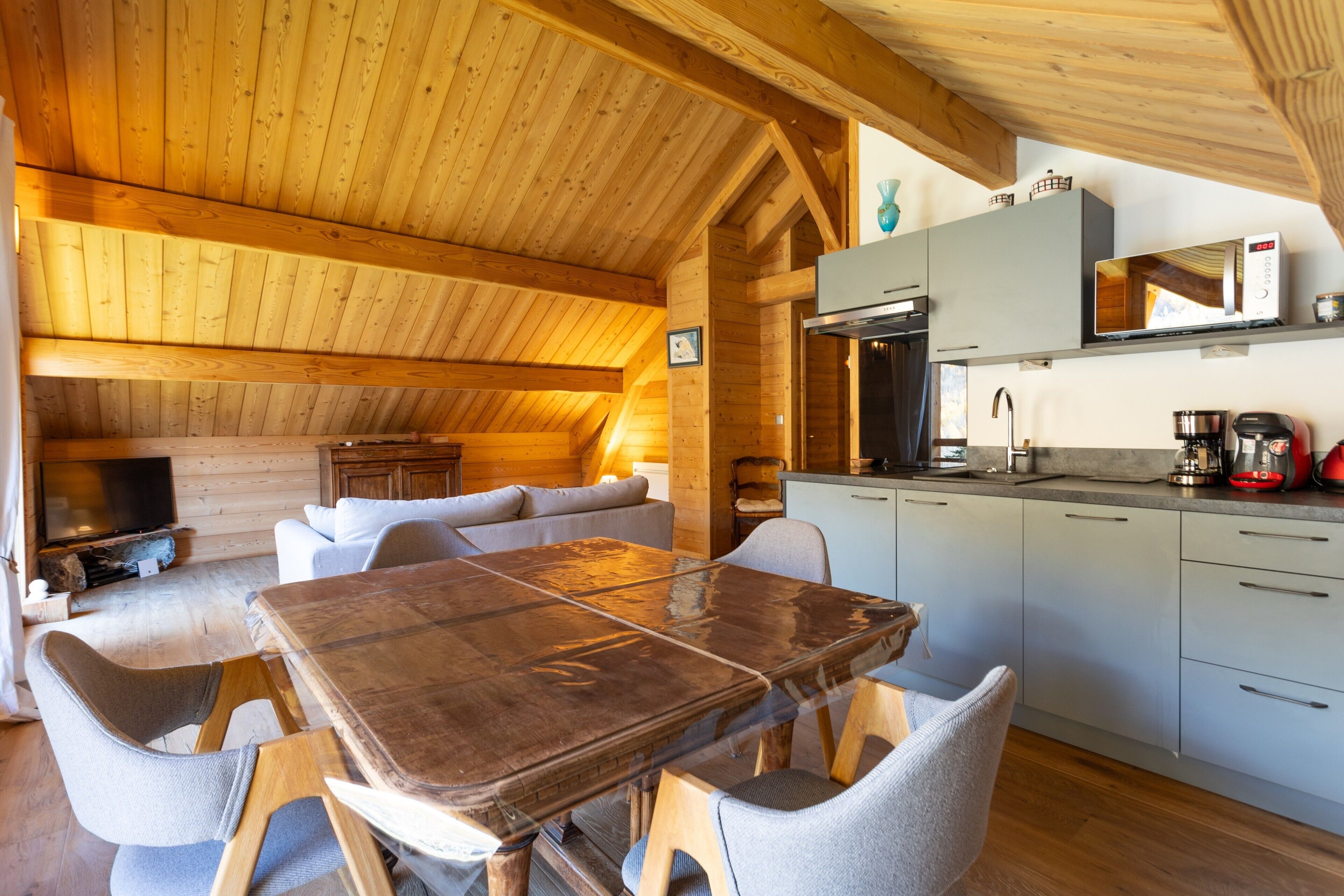 Een houten interieur met een eettafel, stoelen, een keukenhoek en een televisie.