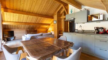 Een houten interieur met een eettafel, stoelen, een keukenhoek en een televisie.
