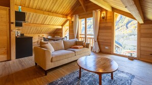 L’intérieur chaleureux d’un chalet en bois comprend un canapé, une table à manger, un coin cuisine et de grandes fenêtres qui offrent une vue sur l’extérieur.