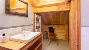 Une salle de bain rustique, située dans une cabane en bois, comprenant un lavabo, un miroir et une chaise en bois.