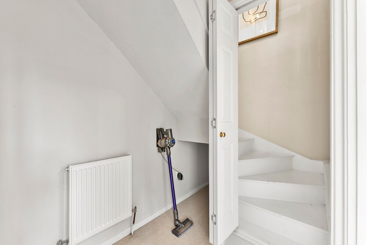 Um quarto com um radiador branco, um aspirador de pó e uma escada que dá para um patamar.