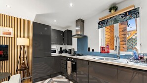 Une cuisine moderne avec des meubles de couleur sombre, une hotte de cuisinière en acier inoxydable, un mur d’accent en bois, un plancher à motifs en chevrons et une fenêtre offrant une vue décorative.