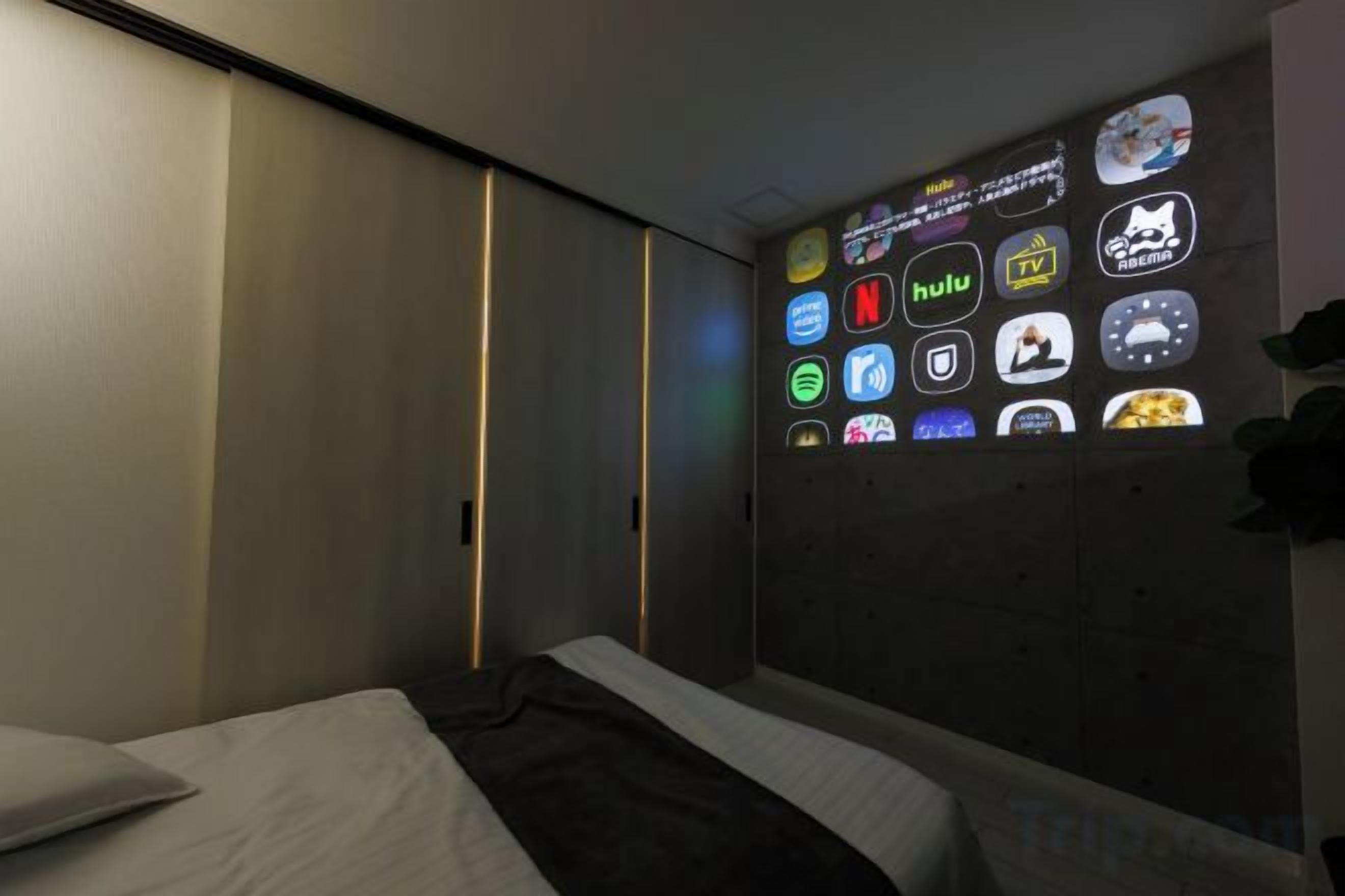 Un dormitorio con cama, un televisor empotrado mostrando varios iconos de aplicaciones y una puerta corrediza.