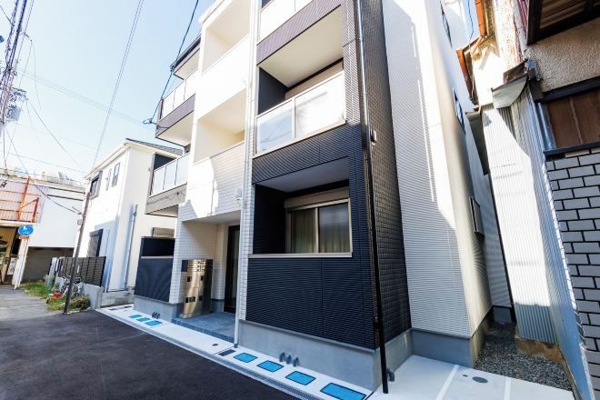 A modern multi-story residential building with balconies, a garage, and a small front yard.