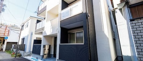 A modern multi-story residential building with balconies, a garage, and a small front yard.